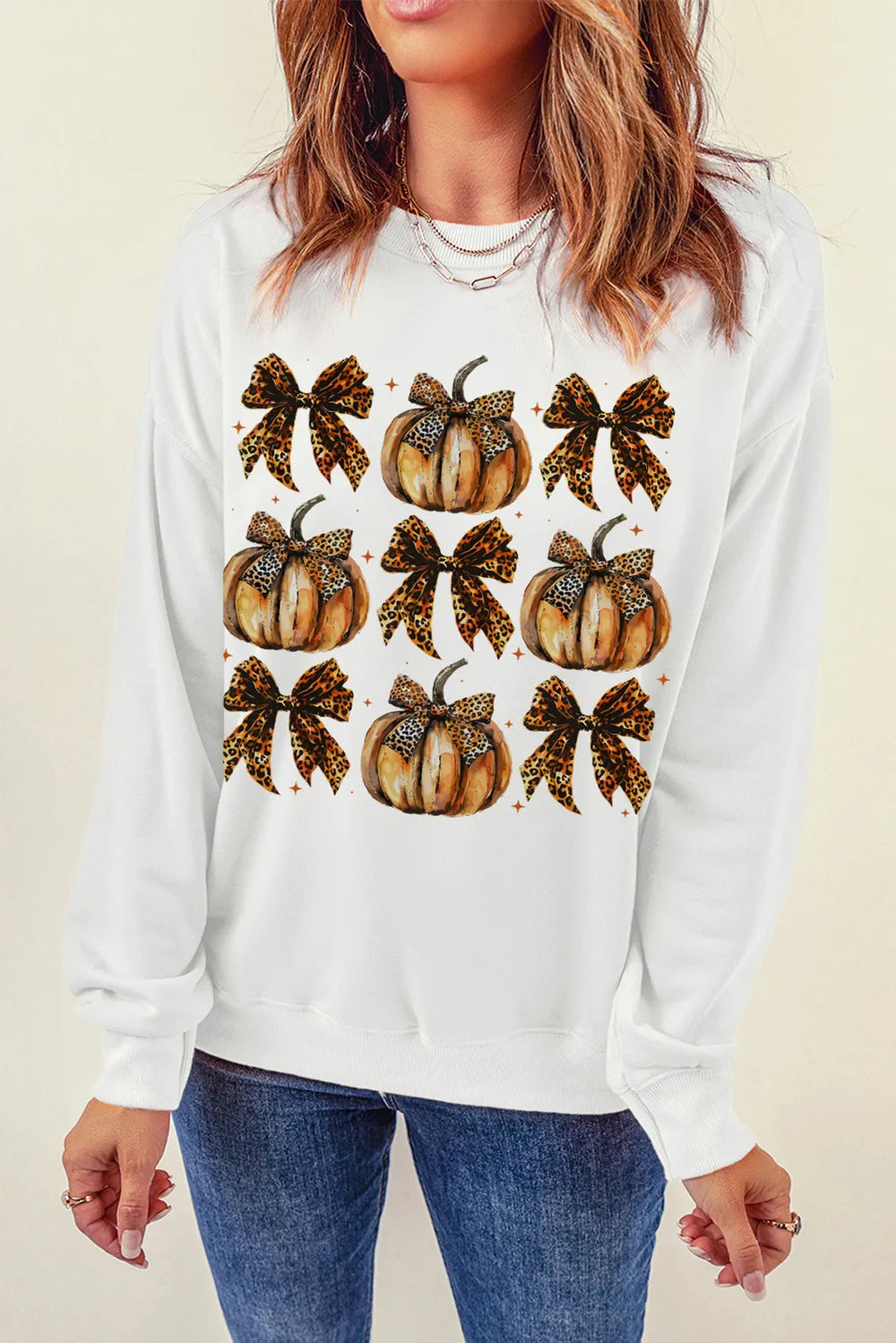 A woman wears a white long-sleeve sweatshirt with a pumpkin and bow graphic.