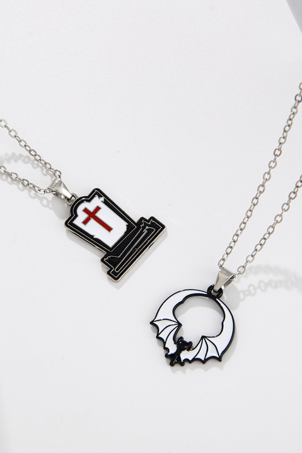 Two silver-toned necklaces, one with a tombstone pendant and one with a bat pendant.