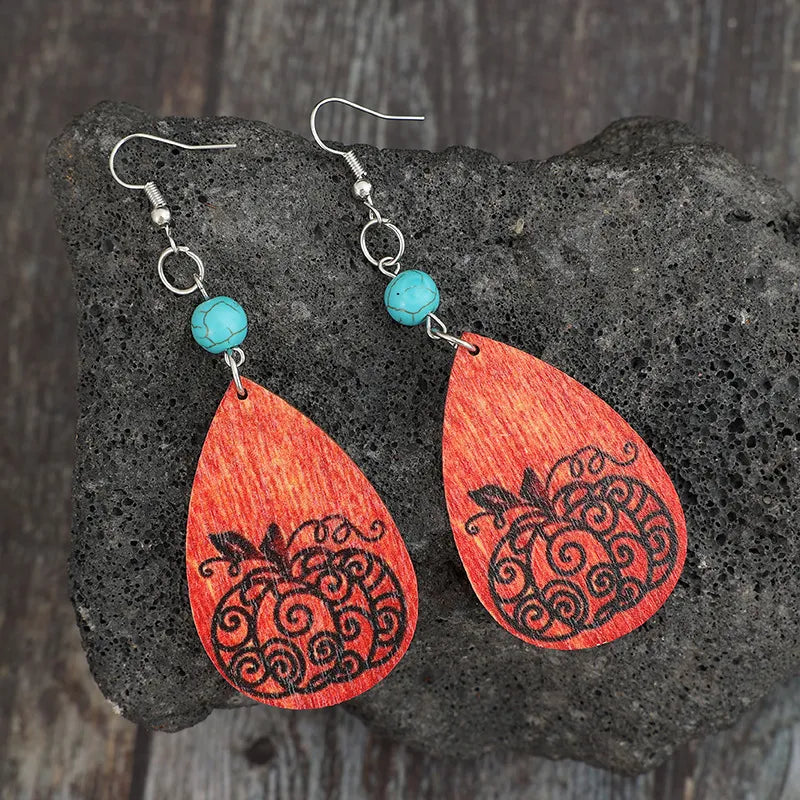 Turquoise wooden pumpkin teardrop earrings on a dark, textured surface.