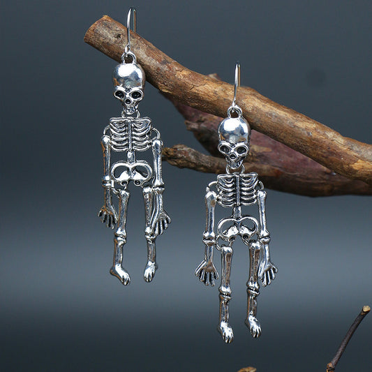 Two silver-colored skeleton alloy earrings hang from a tree branch.