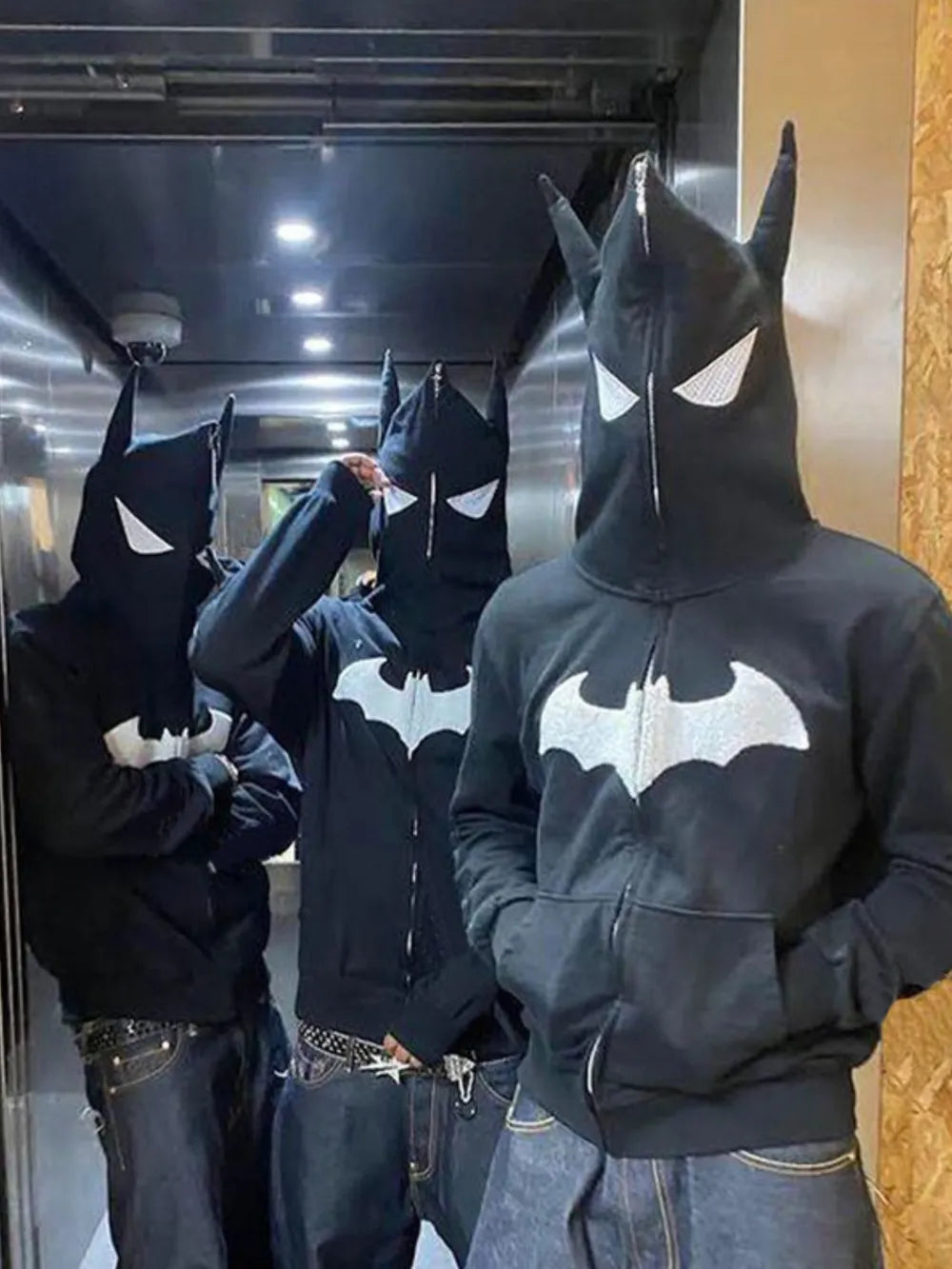 Three men wear black zip-up hoodies with a white bat logo and pointed hoods.