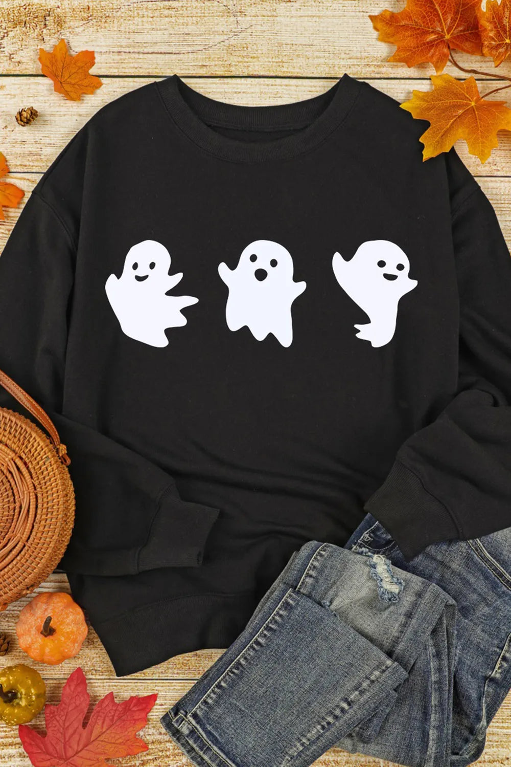 A black long-sleeve sweatshirt with three white ghost figures is displayed with jeans.