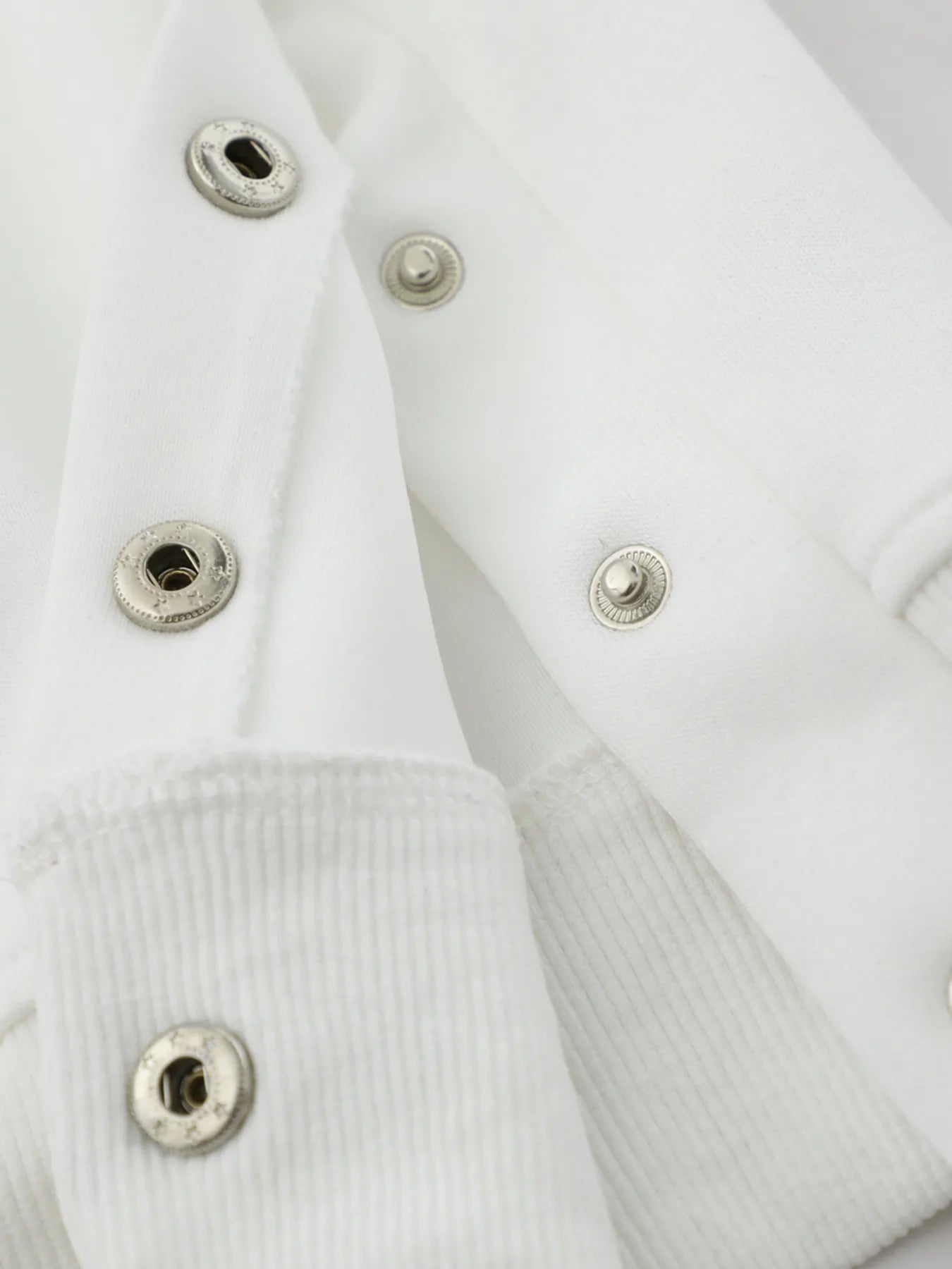 Close-up of a white hoodie with silver snap buttons and ribbed cuffs.