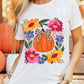 A woman wears a white t-shirt with a pumpkin and floral graphic.