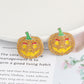 Two rhinestone pumpkin earrings with green stems and yellow faces with red eyebrows.