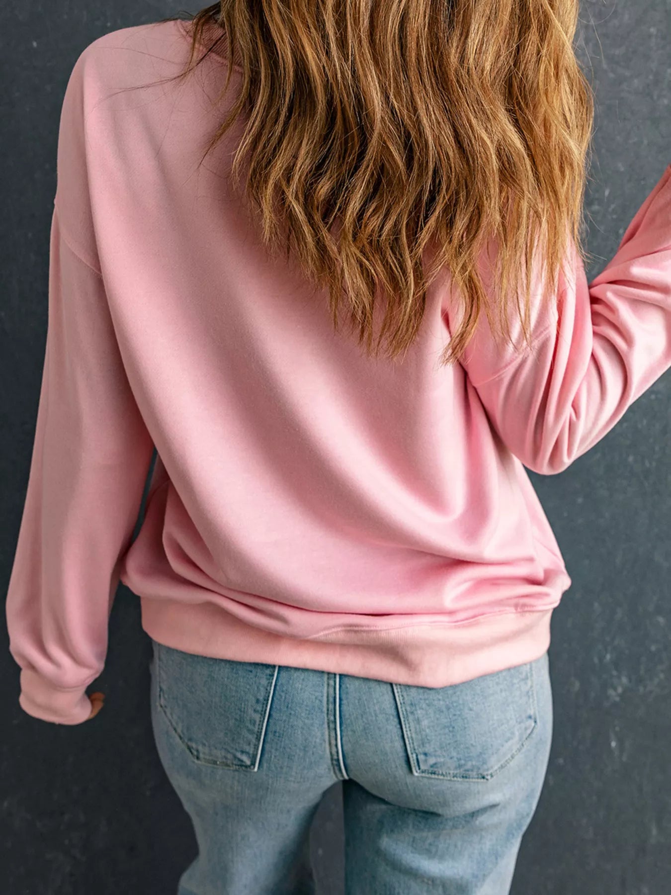 Back view of a woman wearing a pink sweatshirt and blue jeans.