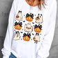 A woman wears a white long-sleeve sweatshirt with pumpkin and ghost designs.