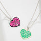 Two heart-shaped necklaces, one pink and one green, both with a spiderweb design.