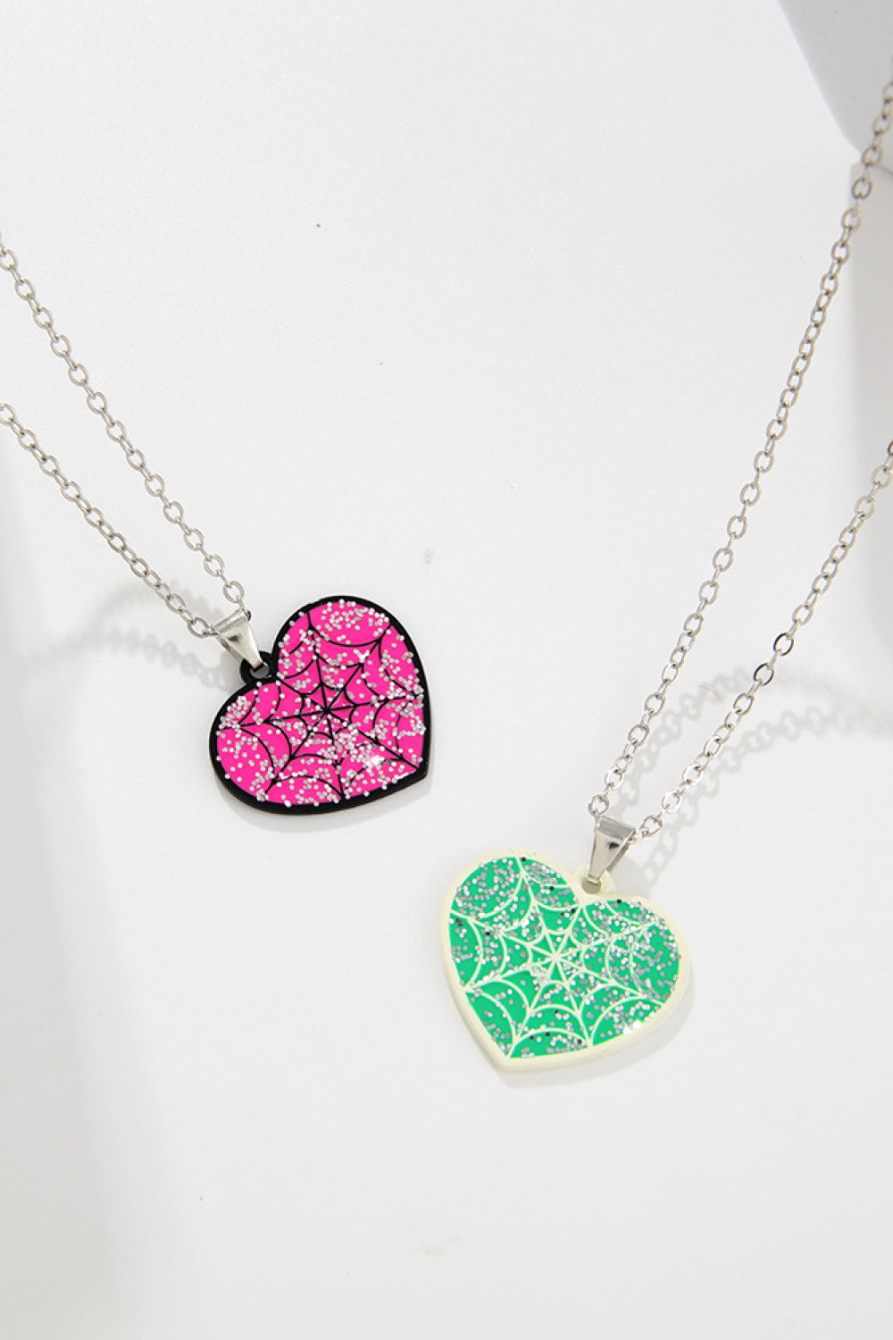 Two heart-shaped necklaces, one pink and one green, both with a spiderweb design.