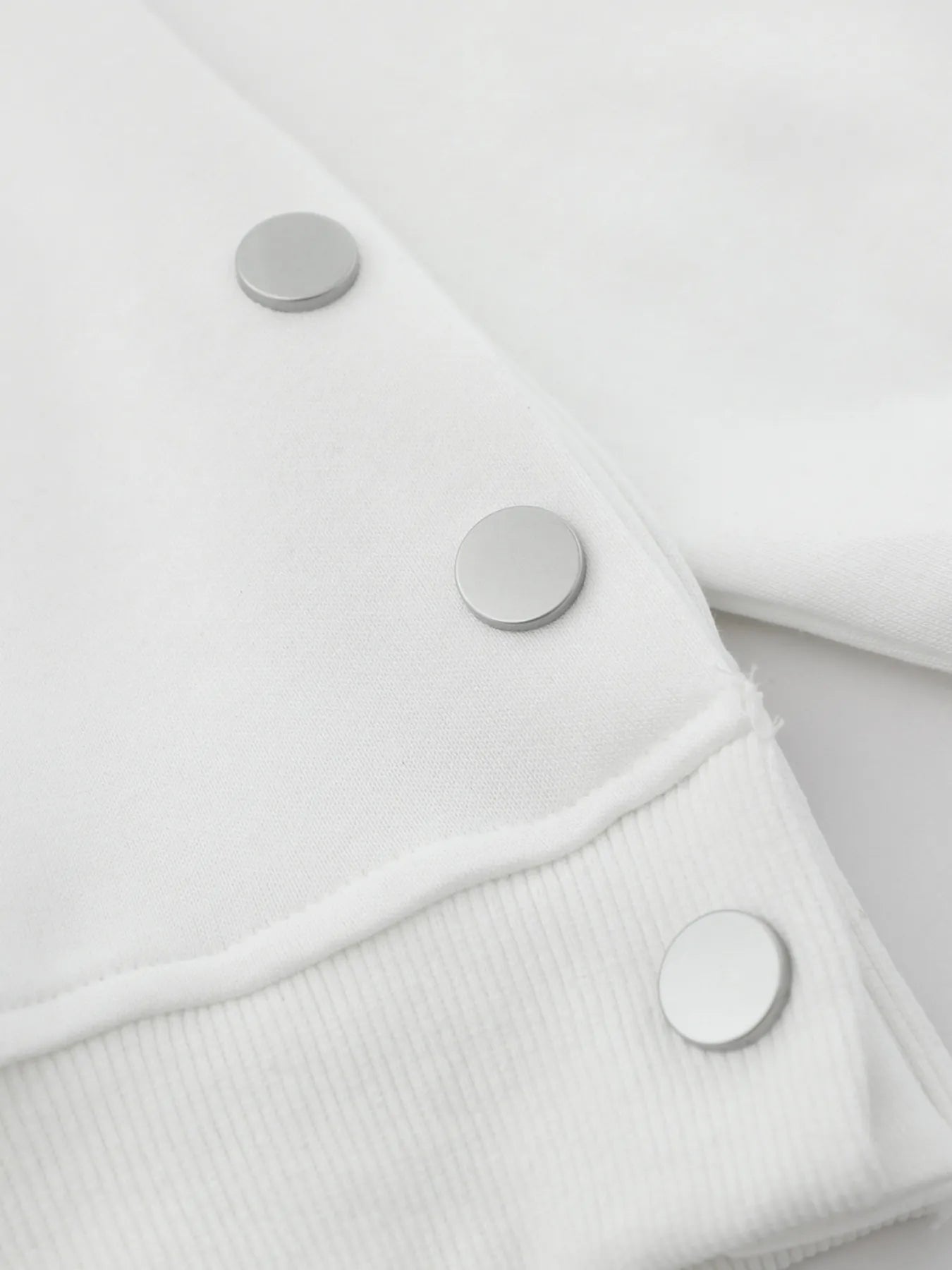 Close-up of a white hoodie with three silver side buttons.