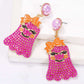 Two pink ghost-shaped earrings with orange bows and smiling faces.