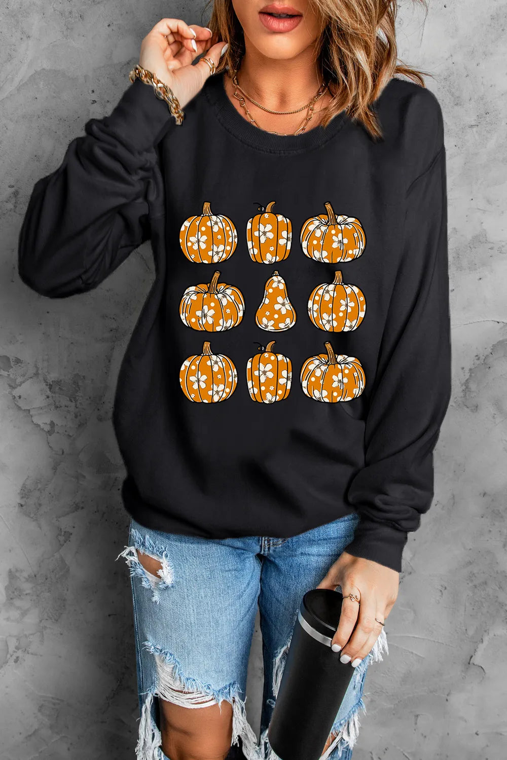 Black long-sleeve sweatshirt with a pumpkin print, worn by a person in ripped jeans.