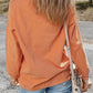 A woman from behind wears an orange corduroy long-sleeve top and blue jeans.