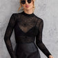 A woman models a black sheer spider web print long sleeve blouse and a black skirt.