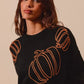 A woman models a black sweater with orange pumpkin embroidery.