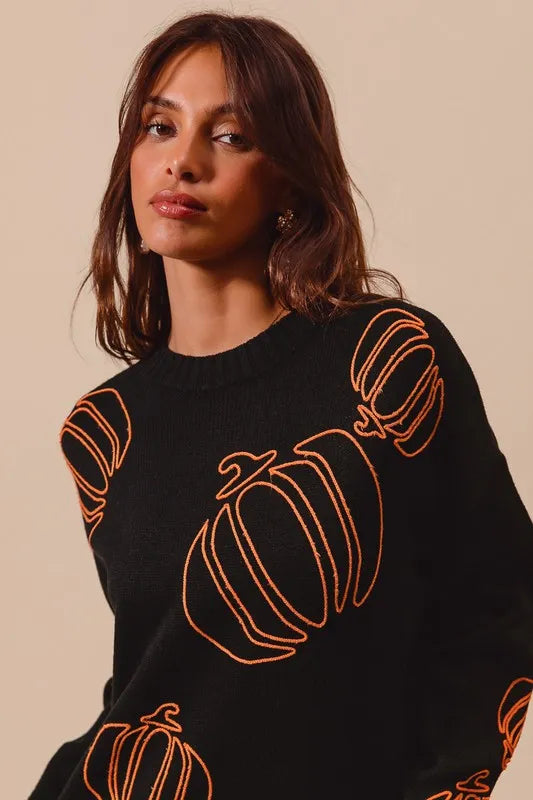 A woman models a black sweater with orange pumpkin embroidery.