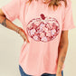A woman wears a pink t-shirt with a floral pumpkin graphic and blue jeans.
