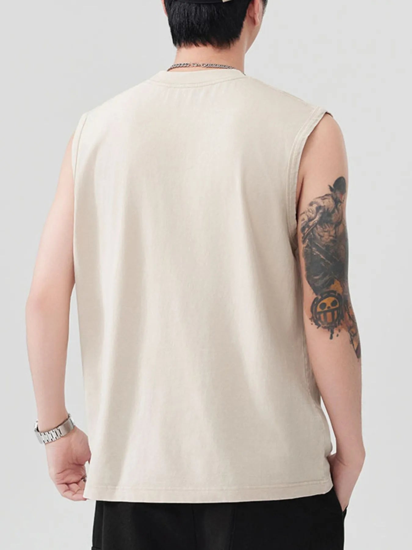 Rear view of a man wearing a beige sleeveless tank top and black pants.
