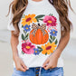A woman wears a white t-shirt with a pumpkin and floral graphic, and denim shorts.