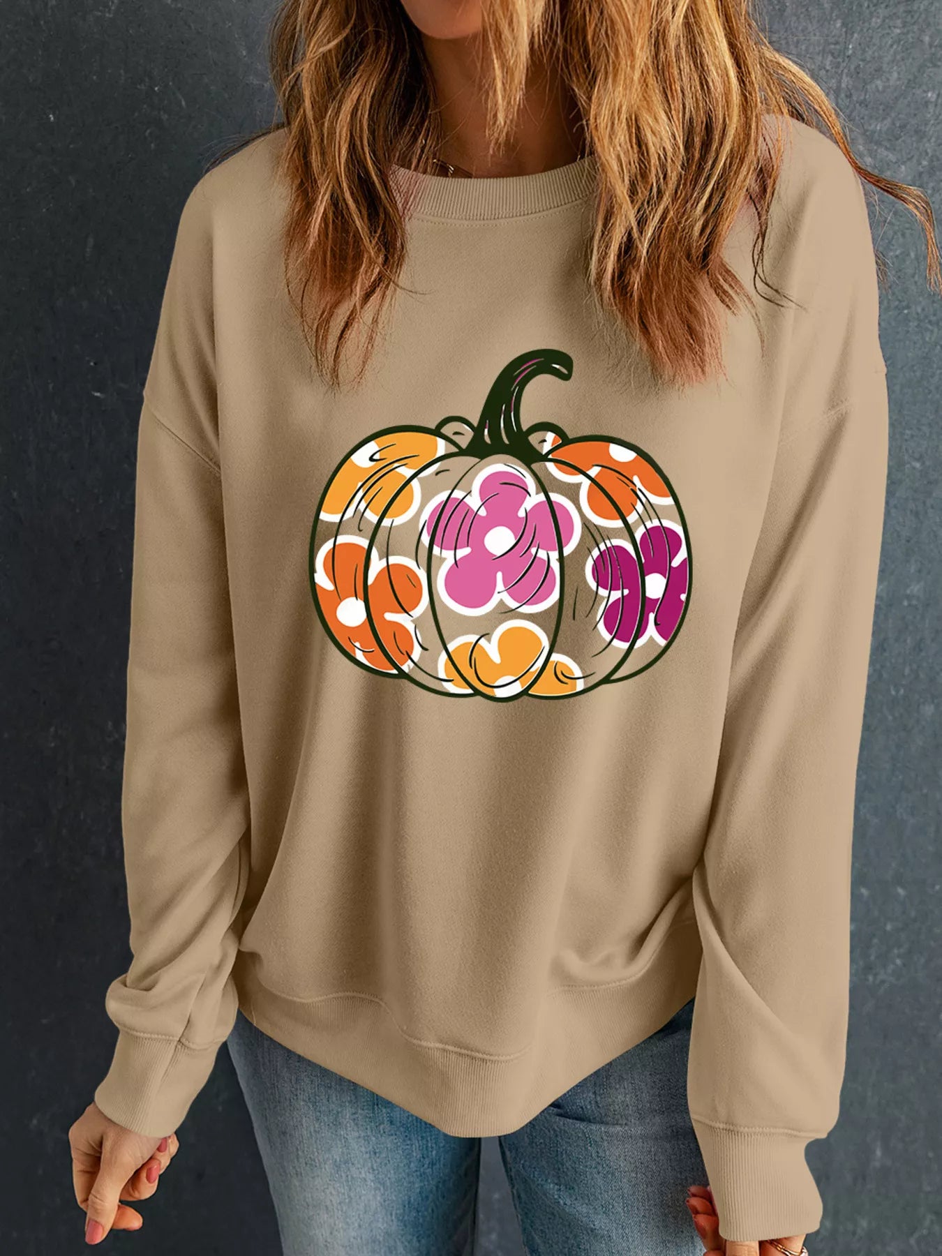 A woman wears a beige drop-shoulder sweatshirt with a colorful floral pumpkin graphic.