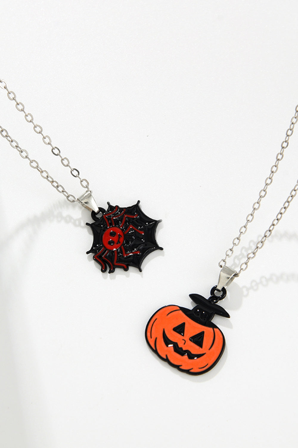 Two Halloween-themed necklaces, one with a spiderweb and spider, the other a pumpkin.