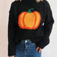 Black cable-knit turtleneck sweater with an orange pumpkin applique, paired with blue jeans.