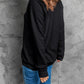 A woman from the back wearing a black long-sleeve sweatshirt and blue jeans.
