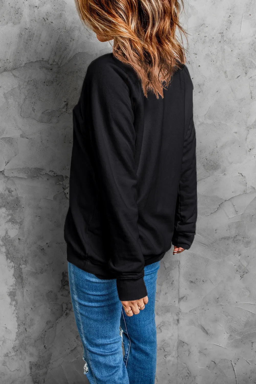 A woman from the back wearing a black long-sleeve sweatshirt and blue jeans.