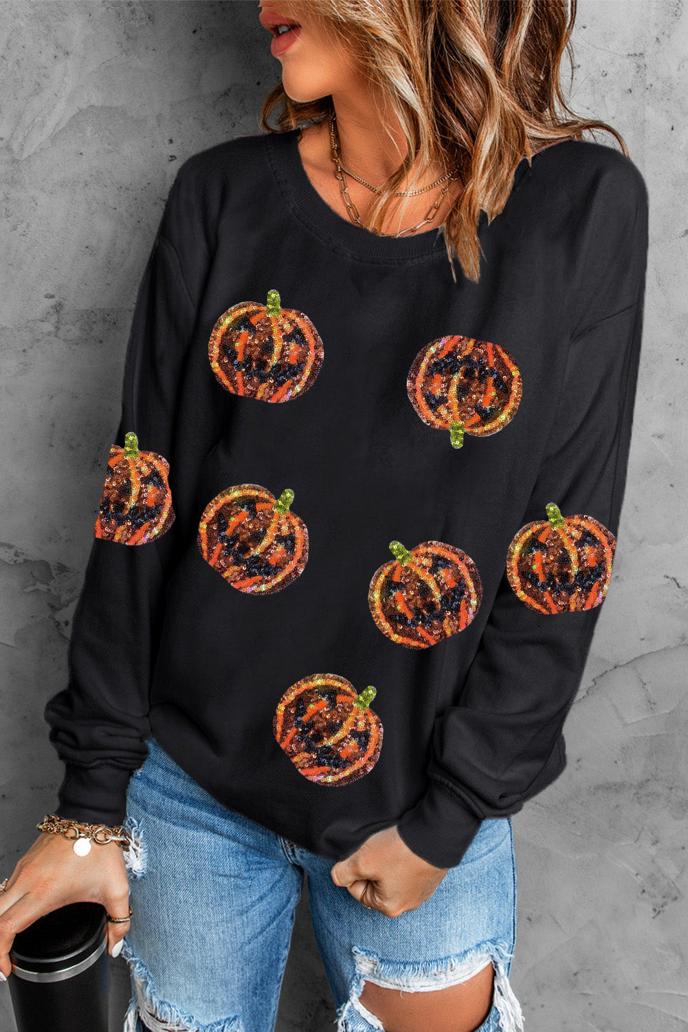 A woman wears a black dropped shoulder sweatshirt with glittery pumpkin designs.