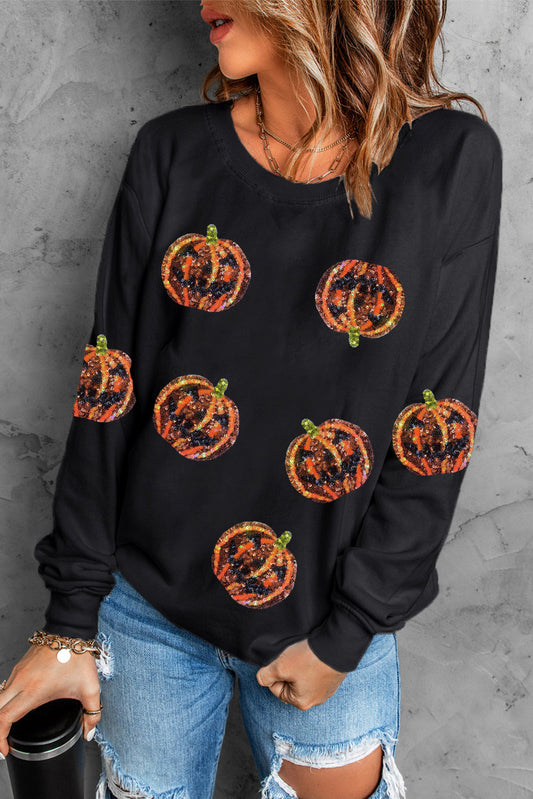 A woman wears a black dropped shoulder sweatshirt with glittery pumpkin designs.