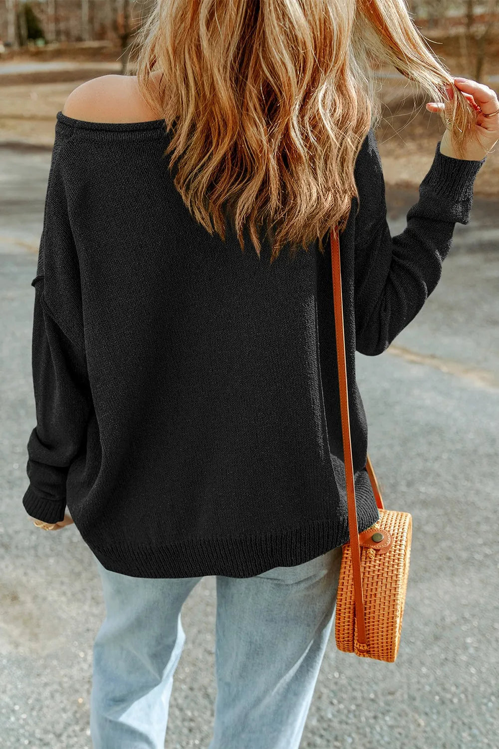 A woman from behind wears a black knit top with an off-the-shoulder neckline.