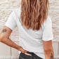 A woman with long wavy hair wears a white short-sleeve tee and dark jeans.