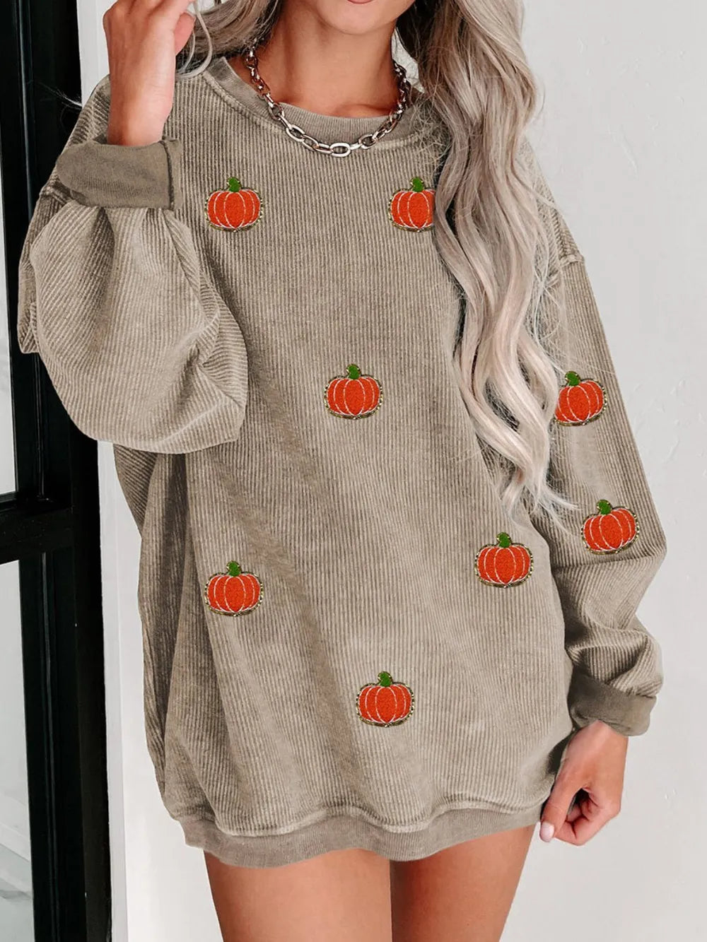 A woman wears a beige corduroy long-sleeve sweatshirt with pumpkin appliques.