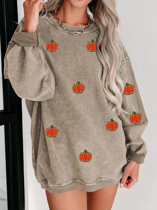 A woman wears a beige corduroy long-sleeve sweatshirt with pumpkin appliques.