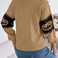 A woman from behind wears a tan pumpkin round neck long sleeve sweater and jeans.