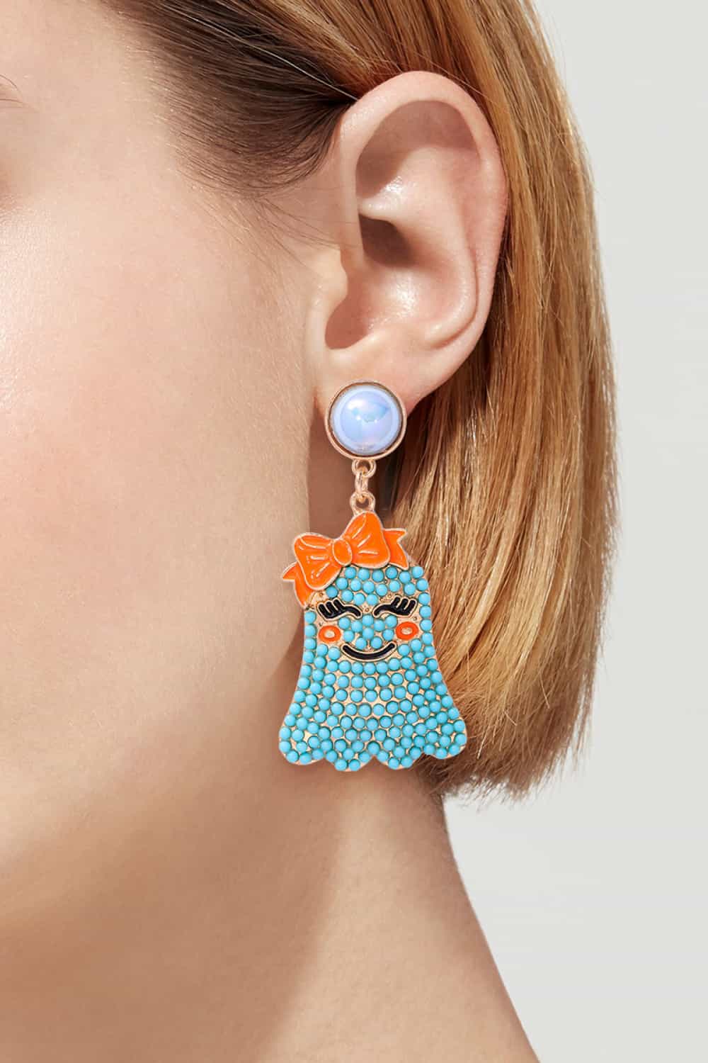 Smiling ghost shape synthetic pearl earrings with an orange bow.