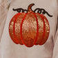 A beige long-sleeve sweatshirt features a large, orange sequin pumpkin design.