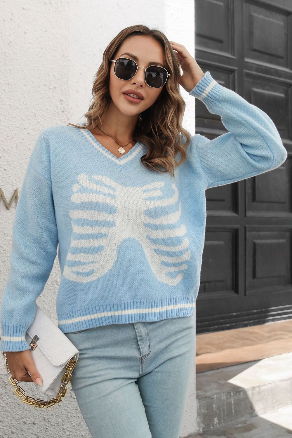 A woman wears a light blue skeleton pattern v-neck long sleeve pullover sweater.