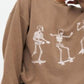 An oversized brown sweatshirt with white skeleton graphics skateboarding.