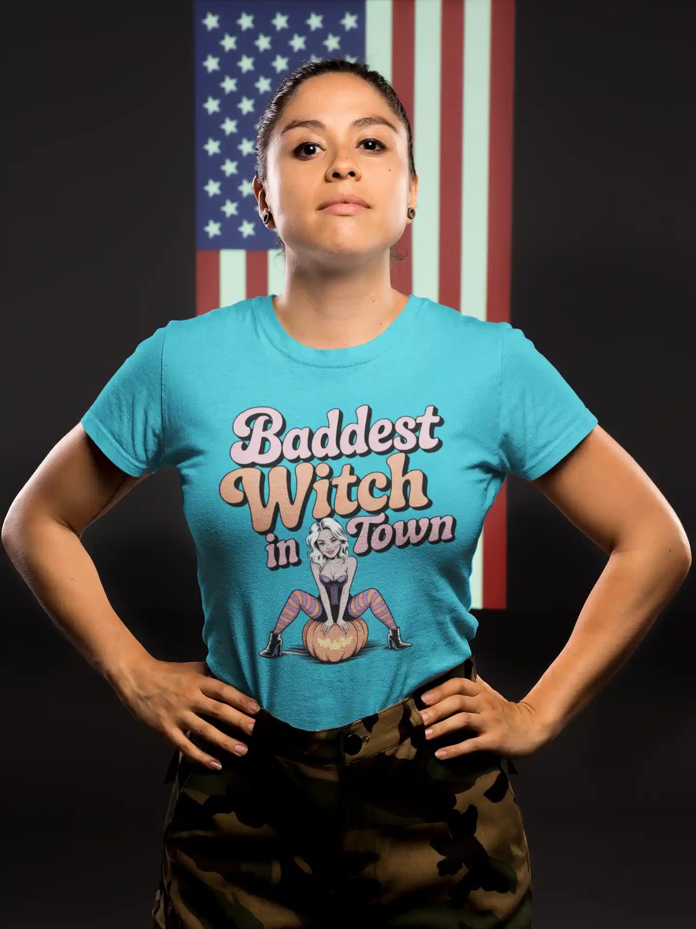 A woman wears a blue t-shirt with "Baddest Witch in Town" and a witch on a pumpkin.