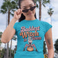 A woman in a teal "Baddest Witch in Town" t-shirt pulls down her sunglasses.