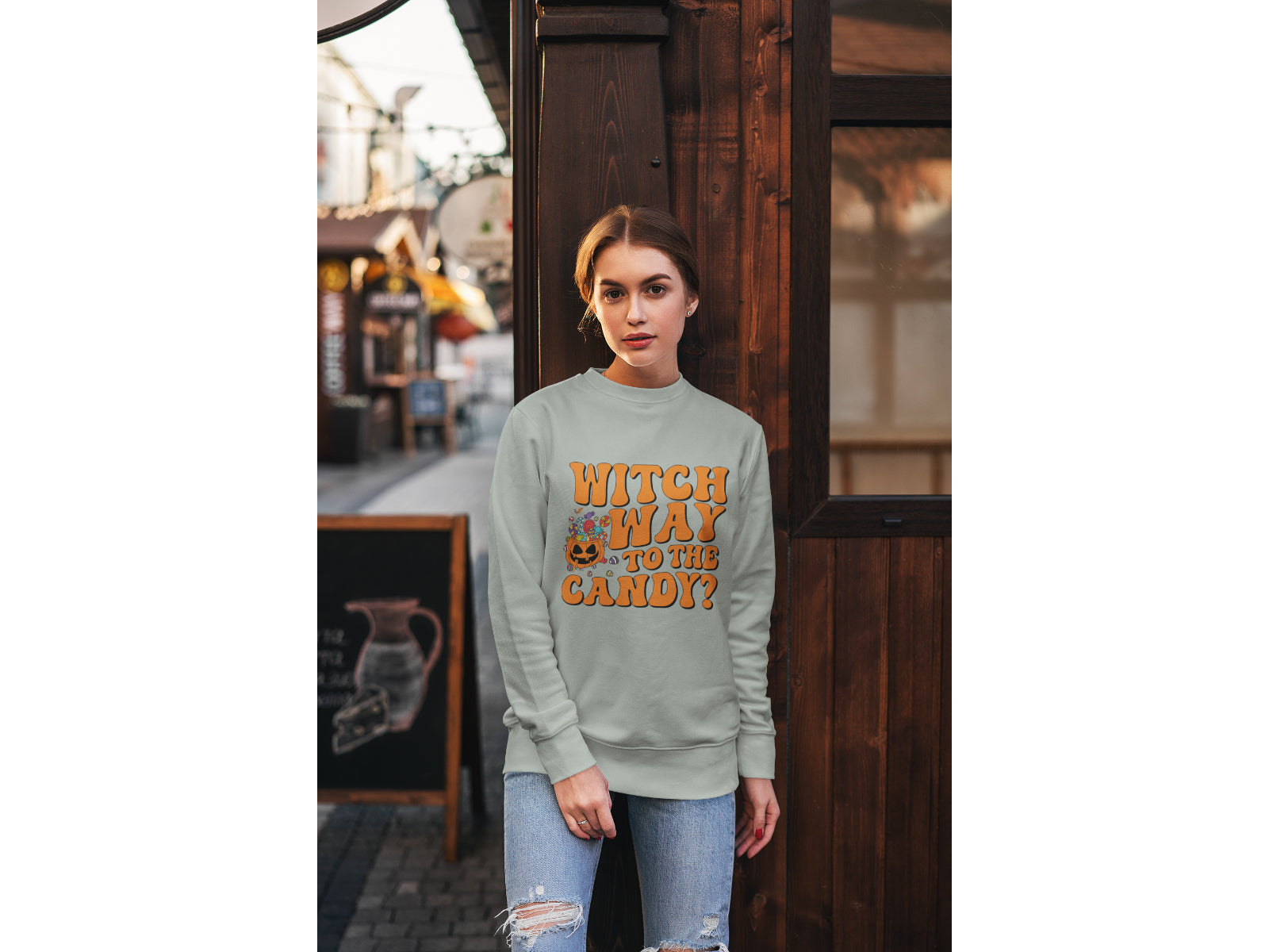 A woman wears a light grey "Witch Way to the Candy" Halloween sweatshirt.