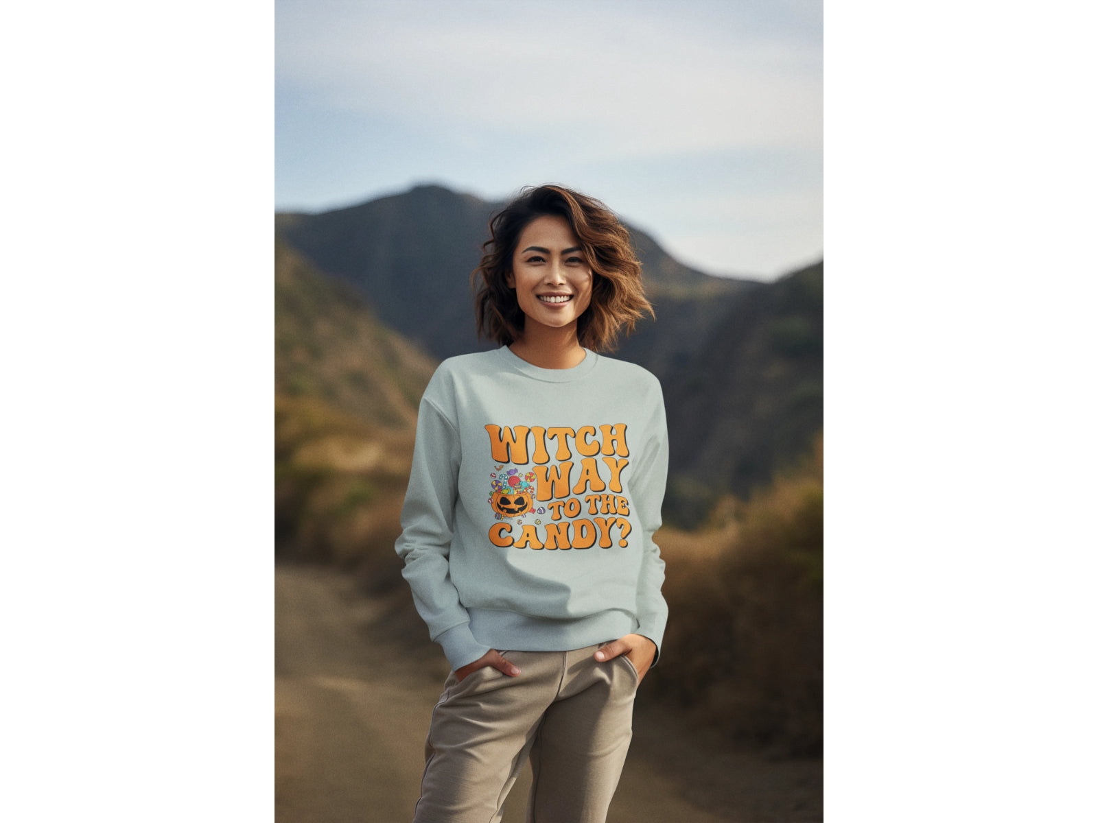 A woman smiles wearing a light blue "Witch Way to the Candy?" Halloween sweatshirt.