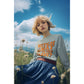 A blonde woman wears a light blue "Witch Way to the Candy" sweatshirt in a field.