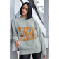 A woman wears a grey sweatshirt with "Witch Way to the Candy?" and a pumpkin graphic.