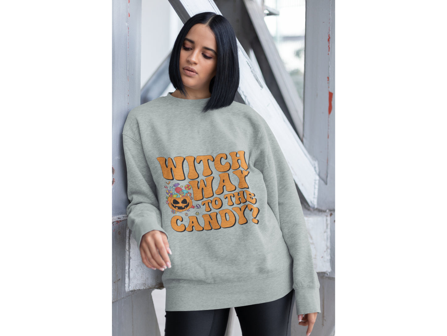 A woman wears a grey sweatshirt with "Witch Way to the Candy?" and a pumpkin graphic.