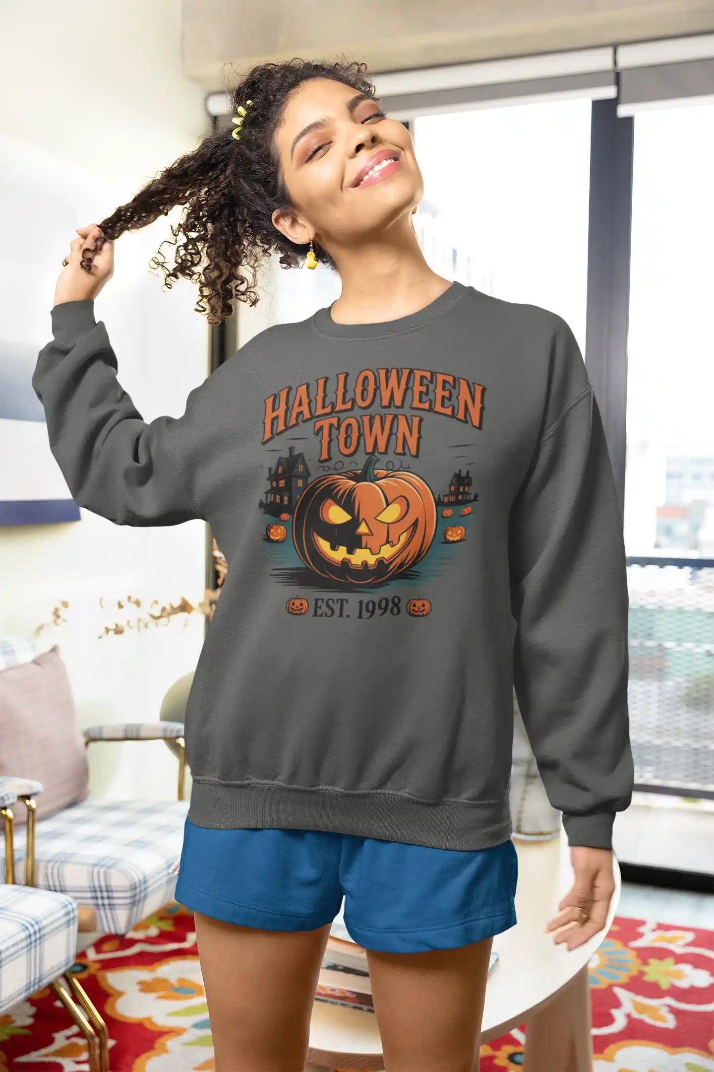 A woman wears a dark gray Halloween Town sweatshirt with a pumpkin graphic.