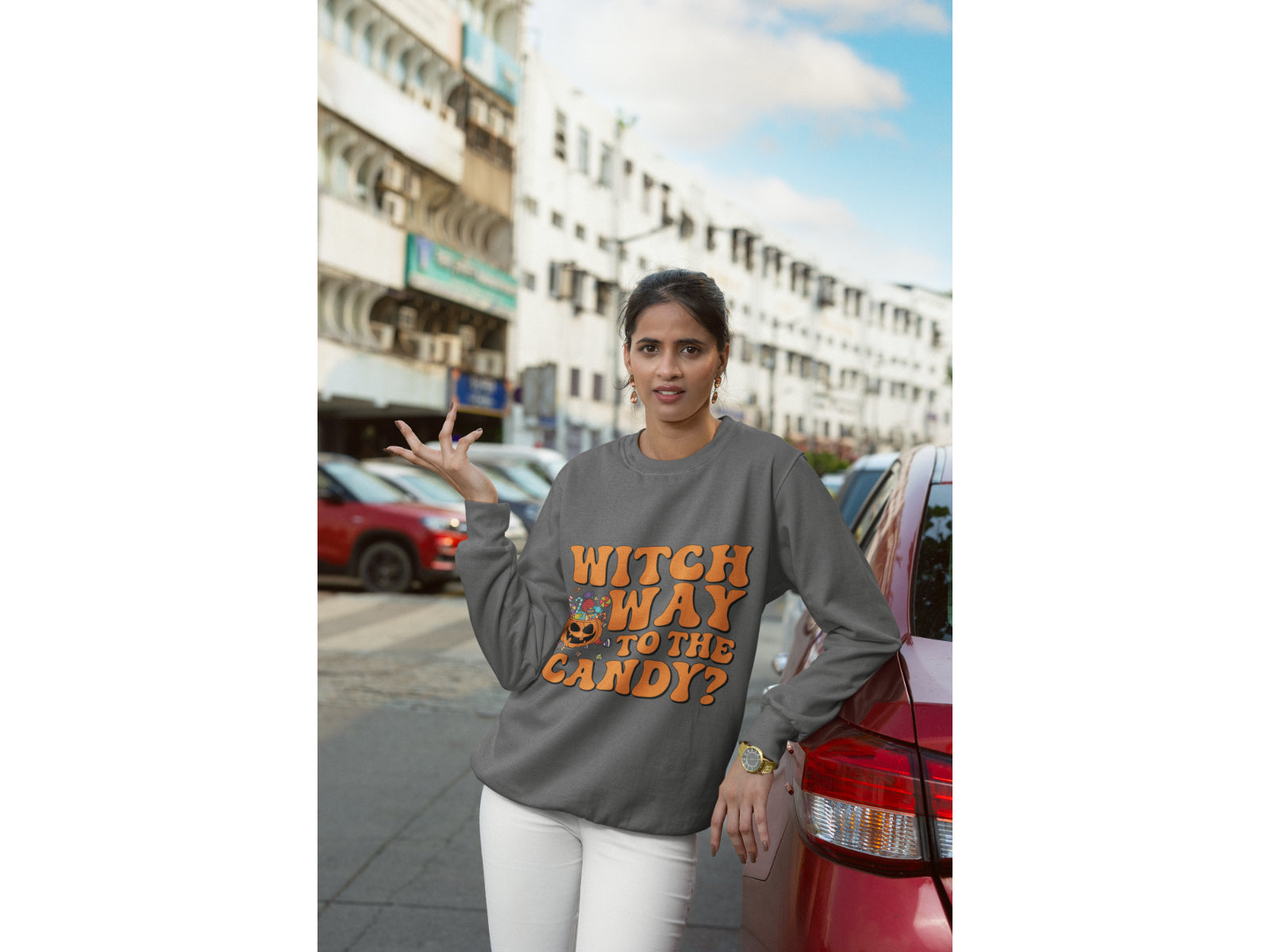 A woman wears a dark gray sweatshirt with "Witch Way to the Candy?" in orange text.