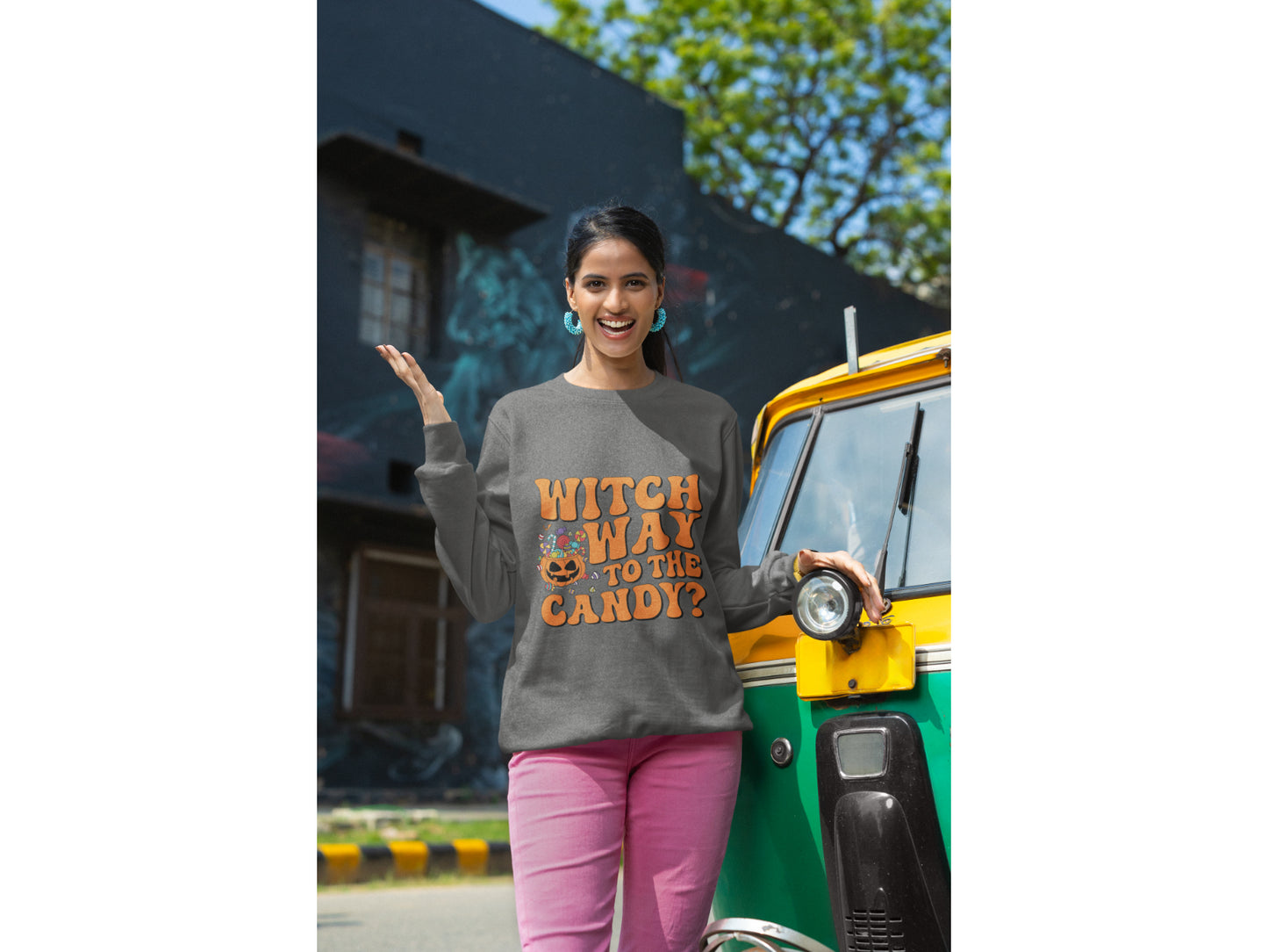 A woman wears a dark gray sweatshirt with "Witch Way to the Candy?" in orange text.