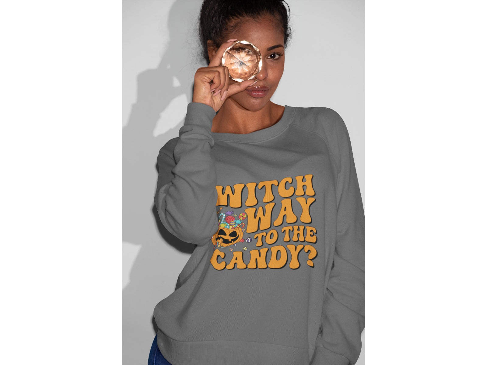 A woman wears a grey "Witch Way to the Candy?" Halloween sweatshirt.